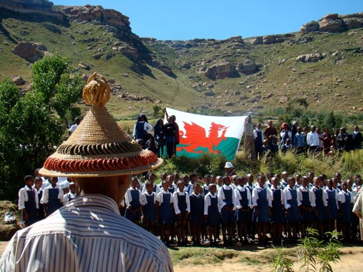Figure in foreground with a hat, school children in background with Welsh flag